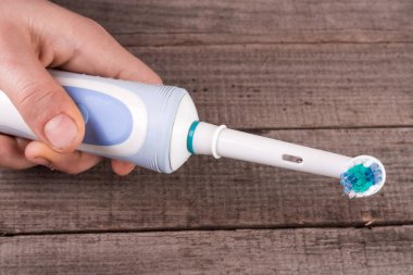 Eski bir ahşap zemin üzerinde elinde elektrikli diş fırçası