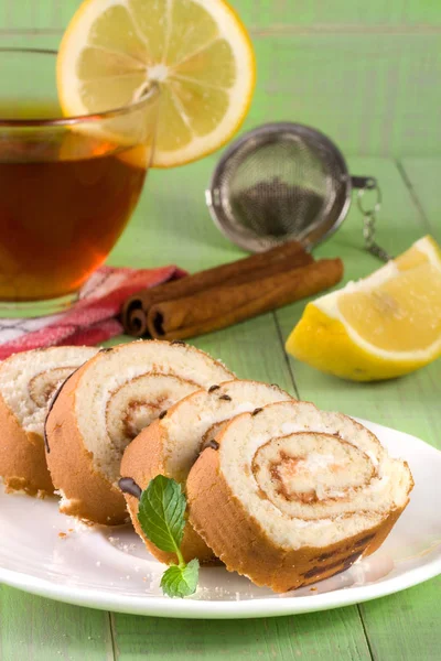 Keksrolle mit einer Tasse Tee auf grünem Holzhintergrund — Stockfoto