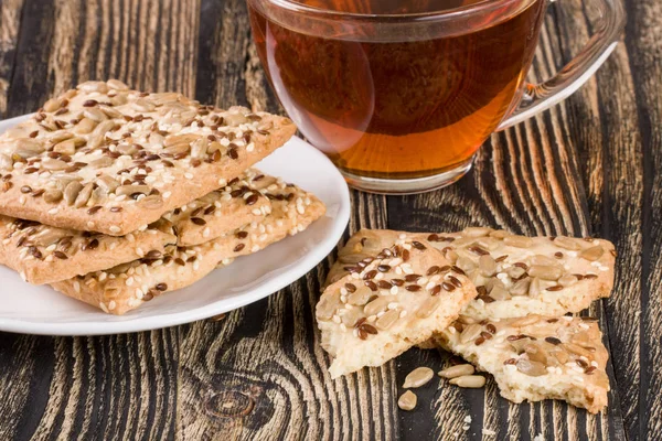 Хрустящий хлеб с семенами подсолнечника, льна и кунжута с чашкой чая на темном деревянном фоне — стоковое фото