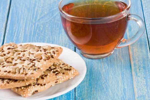 Pain croustillant avec des graines de tournesol, de lin et de sésame avec une tasse de thé sur fond de bois bleu — Photo