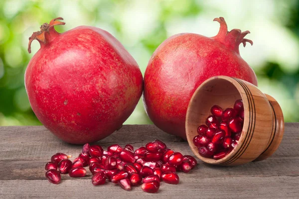 Two pomegranate and garnet grains in a bowl on wooden table with blurred garden background — Stock Photo, Image