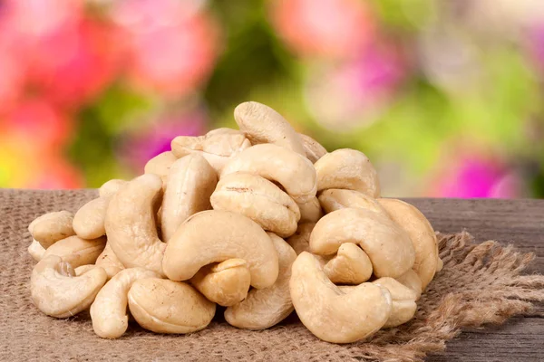 Heap of cashew nuts on a wooden table with sacking and blurred garden background — Stock Photo, Image