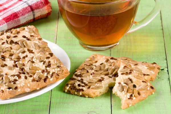 Хрустящий хлеб с семенами подсолнечника, льна и кунжута с чашкой чая на зеленом деревянном фоне — стоковое фото
