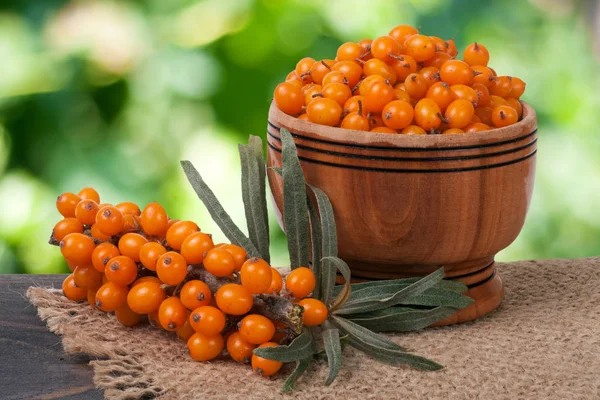 Sanddornbeeren in einer hölzernen Schüssel auf dem Tisch mit verschwommenem Gartenhintergrund — Stockfoto