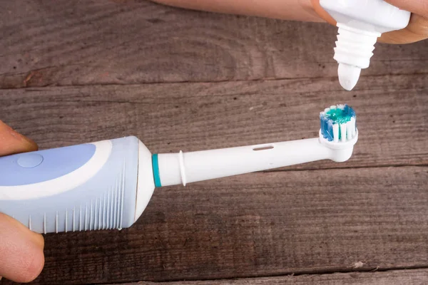 Electric Toothbrush with toothpaste in hand on an old wooden background — Stock Photo, Image