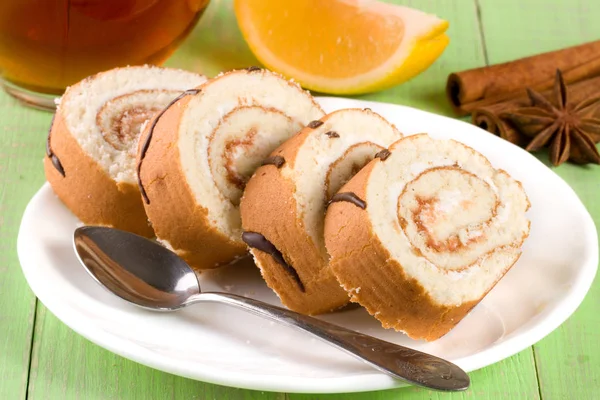 Biscuit swiss roll with a cup of tea on green wooden background — Stock Photo, Image