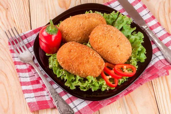 Three fried breaded cutlet with lettuce on a black plate and wooden background — Stock Photo, Image