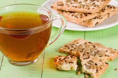 Çıtır çıtır ekmek ile ayçiçeği, keten ve susam tohumu çay yeşil ahşap zemin ile