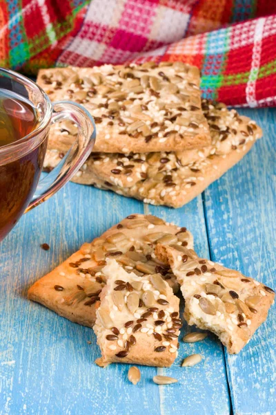 Хрустящий хлеб с семенами подсолнечника, льна и кунжута с чашкой чая на синем деревянном фоне — стоковое фото
