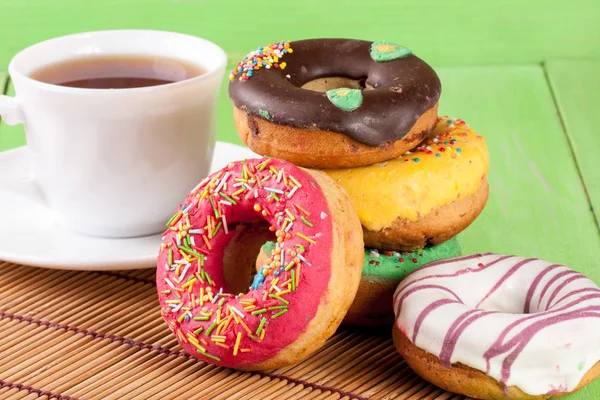 Stapel geglazuurde donuts met een kopje thee op een groene houten achtergrond — Stockfoto