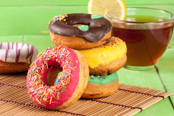 Pile of glazed donuts with a cup of tea on a green wooden background — Stock Photo, Image