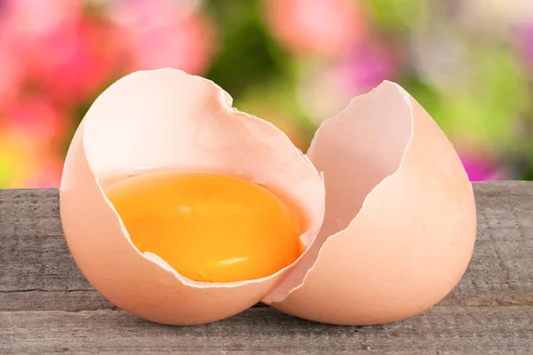 Uovo rotto con tuorlo e guscio d'uovo Su un tavolo di legno con uno sfondo sfocato giardino — Foto Stock