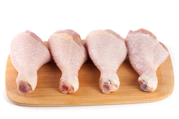 Cuatro palillos de pollo crudos sobre un tablero de corte de madera aislado sobre fondo blanco — Foto de Stock