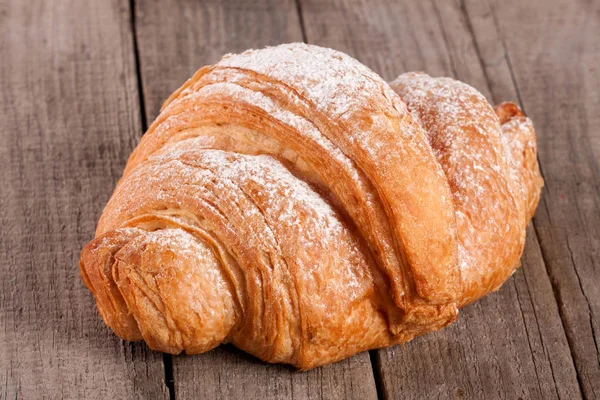 Croissant espolvoreado con azúcar en polvo sobre tabla de madera vieja — Foto de Stock