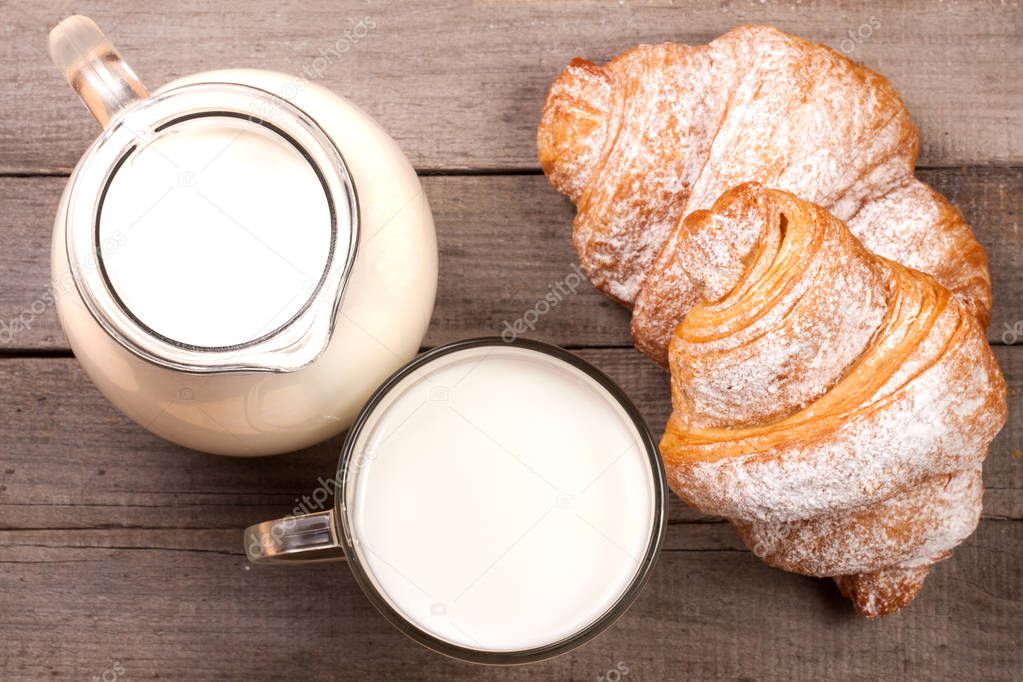 jug and glass of milk with croissants on a wooden background. Top view