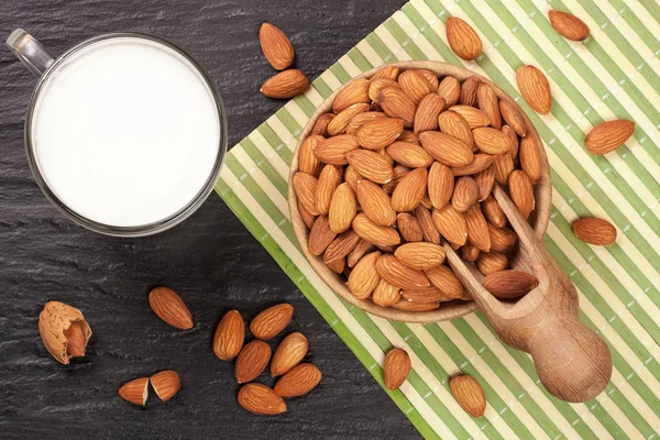 Lait d'amande dans un verre et amandes dans un bol en bois sur fond de pierre noire. Vue du dessus — Photo