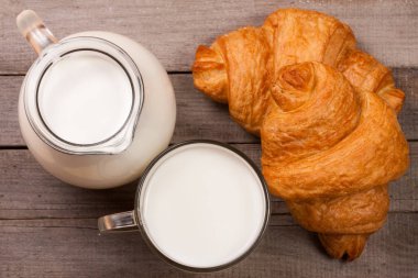 Sürahi ve bir bardak süt ile ahşap bir zemin üzerine bir ay çöreği. Üstten Görünüm