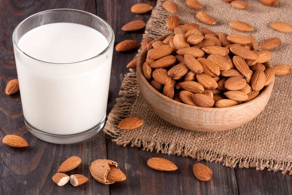 Almond milk in a glass and almonds in a bowl on dark wooden background — Stock Photo, Image