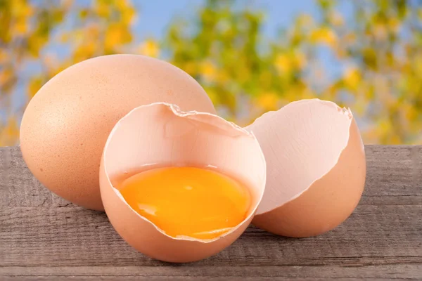 Gebroken ei met eigeel en de "eggshell" op een houten tafel met een wazige achtergrond van tuin — Stockfoto