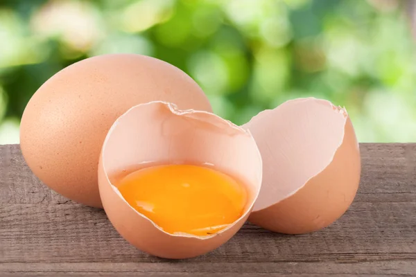 Gebroken ei met eigeel en de "eggshell" op een houten tafel met een wazige achtergrond van tuin — Stockfoto