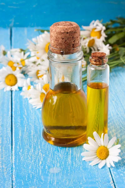 uçucu yağ ve bluewooden arka plan üzerinde taze papatya çiçeği ile şişe