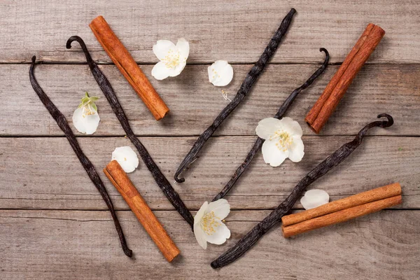 Stik vanili dan kayu manis dengan bunga dan daun pada latar belakang kayu tua — Stok Foto