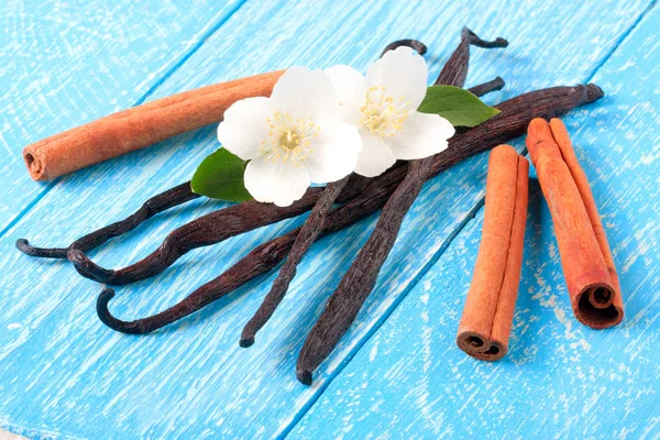Stik vanili dan kayu manis dengan bunga dan daun pada latar belakang kayu biru — Stok Foto