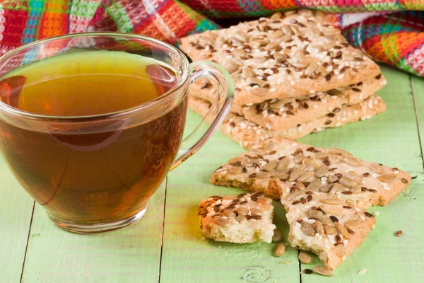 木製の背景が緑色のお茶のカップとひまわり、亜麻と胡麻の種子とシャキッとしたパン — ストック写真