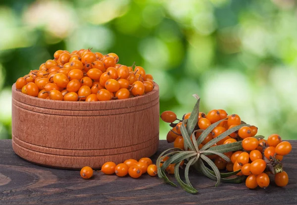 Sanddornbeeren in einer hölzernen Schüssel auf dem Tisch mit verschwommenem Gartenhintergrund — Stockfoto