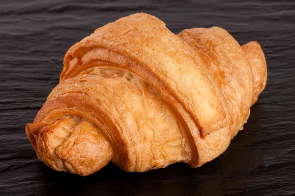 Un croissant su sfondo di pietra nera primo piano — Foto Stock