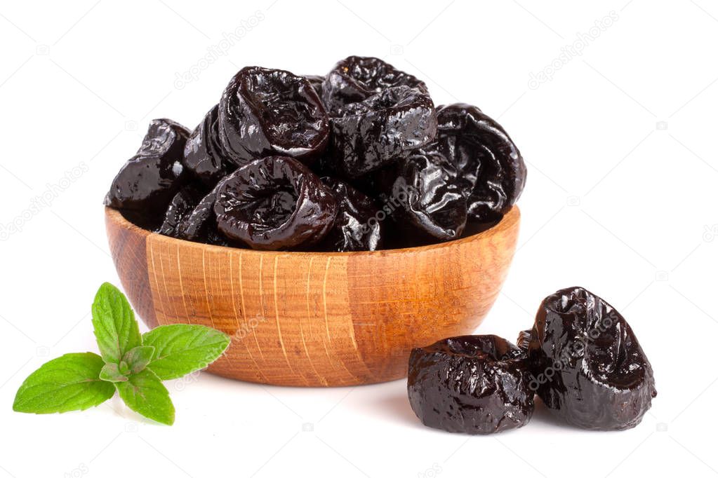 Dried plums or prunes with a mint leaf in wooden bowl isolated on white background
