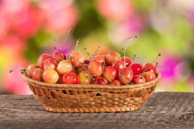 Bulanık bir bahçe arka plan ile ahşap bir masa üzerinde bir hasır sepet içinde sarı kiraz