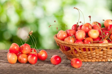 Bulanık bir bahçe arka plan ile ahşap bir masa üzerinde bir hasır sepet içinde sarı kiraz