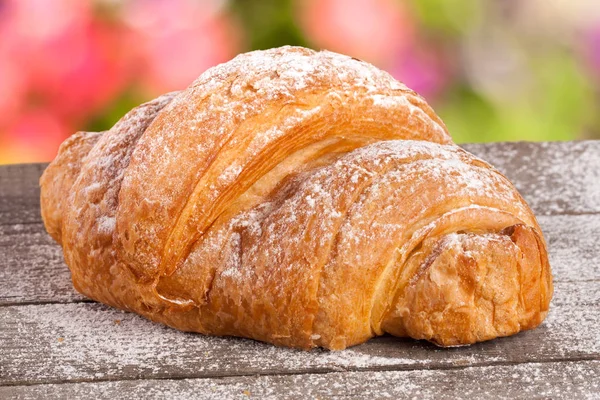 Croissant cosparso di zucchero a velo su una tavola di legno con uno sfondo sfocato giardino — Foto Stock