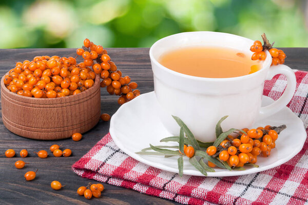 Tea of sea-buckthorn berries on wooden table with blurred garden