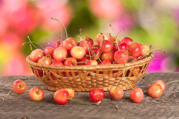 Bulanık bir bahçe arka plan ile ahşap bir masa üzerinde bir hasır sepet içinde sarı kiraz