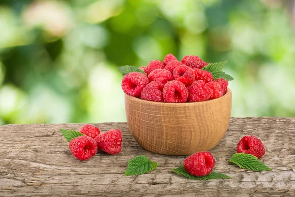 Ahududu bulanık bir bahçe arka plan ile tabloda bir ahşap kase