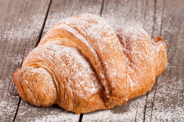 Croissant polvilhado com açúcar em pó na placa de madeira velha — Fotografia de Stock