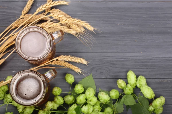 Glas schäumendes Bier mit Hopfenzapfen und Weizen auf schwarzem Holzgrund. Ansicht von oben mit Kopierraum für Ihren Text — Stockfoto