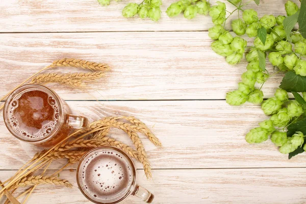 Glas schäumendes Bier mit Hopfenzapfen und Weizen auf weißem Holzgrund. Ansicht von oben mit Kopierraum für Ihren Text — Stockfoto