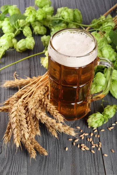 Склянка пінистого пива з шишками хмелю та пшениці на чорному дерев'яному фоні — стокове фото