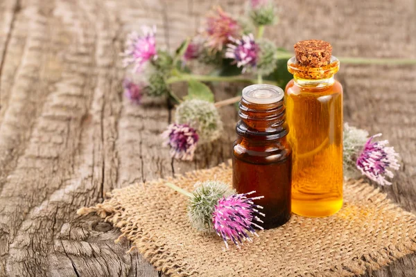 Aceite de bardana en botella de vidrio y flores de bardana sobre un fondo de madera viejo — Foto de Stock