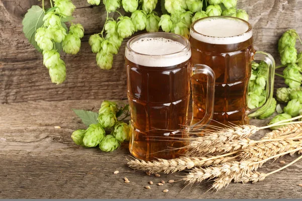 Glas schäumendes Bier mit Hopfendolden und Weizen auf altem Holzgrund — Stockfoto