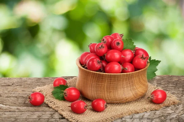 Hawthorn berry yaprak bulanık bir bahçe arka plan ile ahşap masa üzerinde bir kase ile