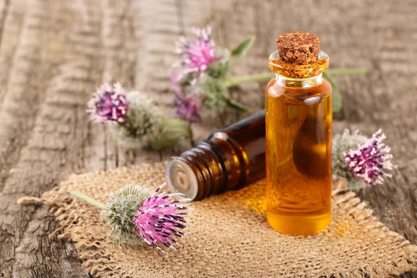 Klit olie in glazen fles en klit bloemen op een oude houten achtergrond — Stockfoto