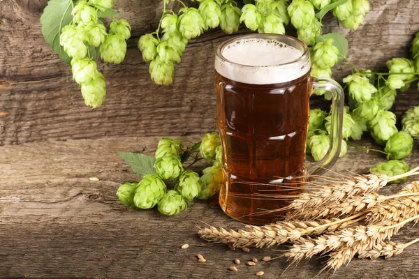 Склянка пінистого пива з шишками хмелю і пшениці на старому дерев'яному фоні — стокове фото