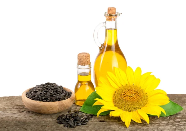 Подсолнечное масло, семена и цветок на деревянном столе на белом фоне — стоковое фото