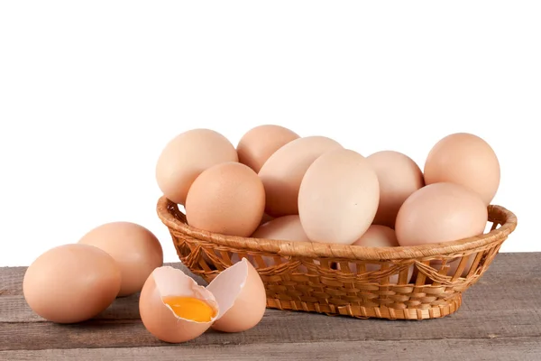 Яйца на деревянном столе в плетеной корзине на белом фоне — стоковое фото