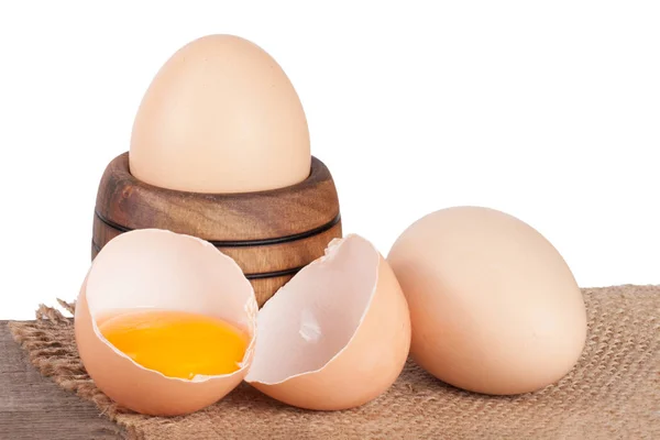 Gebroken ei met eigeel en de "eggshell" op een houten tafel met een witte achtergrond — Stockfoto