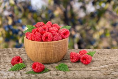 Ahududu bulanık bir bahçe arka plan ile tabloda bir ahşap kase